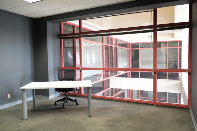 Standard sized office with table, desk, and red-framed window.